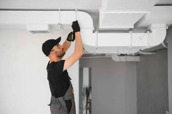 HVAC technician inspecting overhead ductwork in a clean residential space